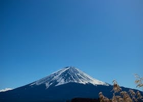 Scenic view of snow-capped Mount Fuji with a tranquil lake in the foreground under a clear blue sky.